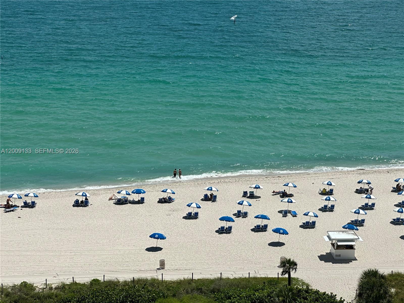 An aerial view shows a sandy beach with blue umbrellas and people near the ocean — 6039 Collins Ave # 1510, Miami Beach FL 33140, MIAMI BEACH, FL