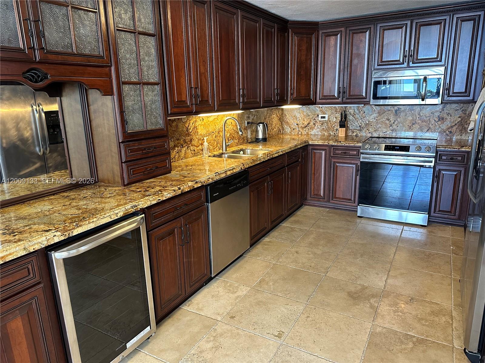 A kitchen features dark wood cabinets, granite countertops, stainless steel appliances, and tiled flooring — 6039 Collins Ave # 1510, Miami Beach FL 33140, MIAMI BEACH, FL