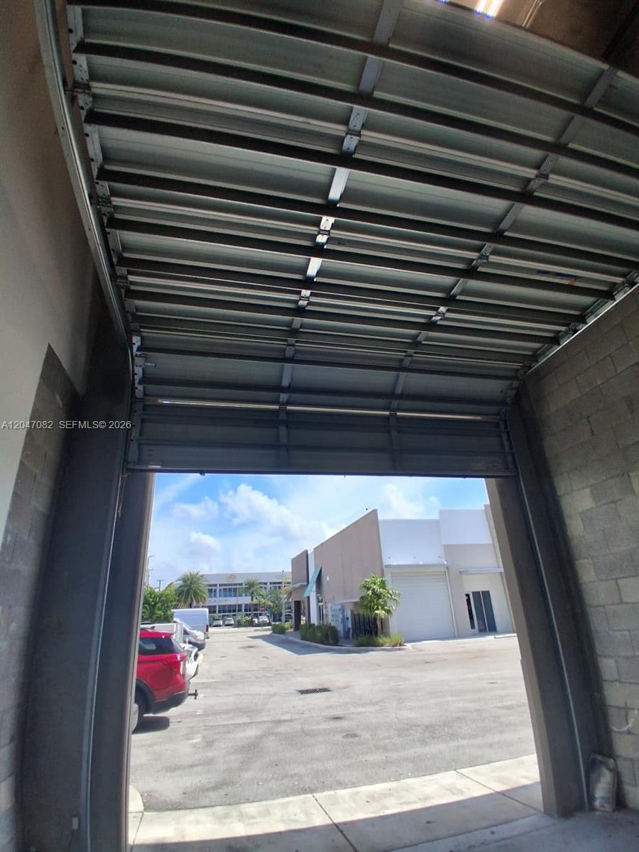 A view looking out from an open industrial garage door toward a parking lot — SWEETWATER, FL