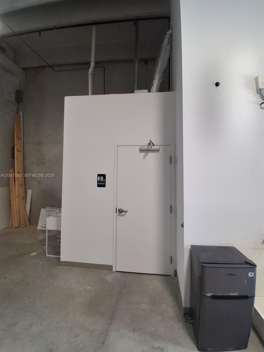 A white door with a restroom sign is set in a room with concrete floors — SWEETWATER, FL
