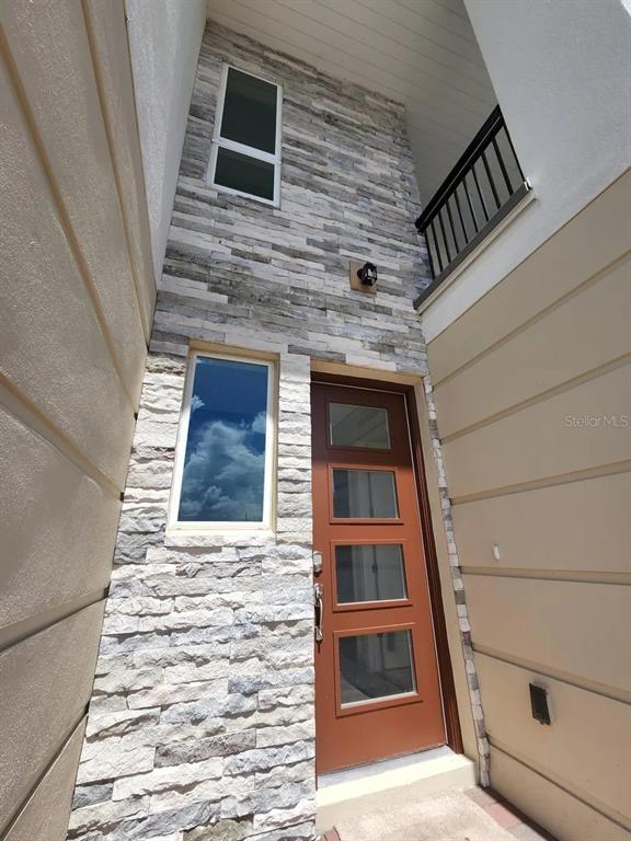 A modern entryway features a brown door with glass panels and a stacked stone facade — 13647 LARKTON LANE, ORLANDO, FL