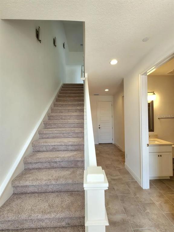 A carpeted staircase leads upward next to a tiled hallway with a bathroom entrance — 13647 LARKTON LANE, ORLANDO, FL