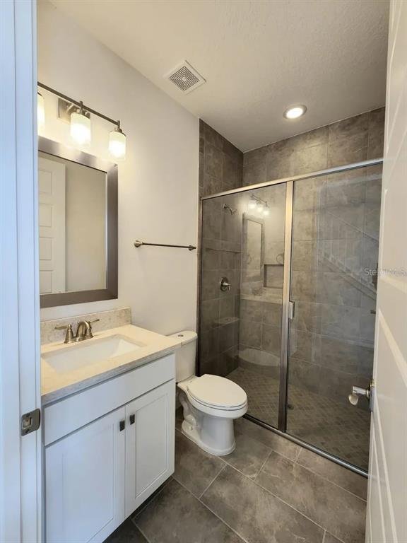 A bathroom features a white vanity, a toilet, and a glass-enclosed shower with gray tiles — 13647 LARKTON LANE, ORLANDO, FL