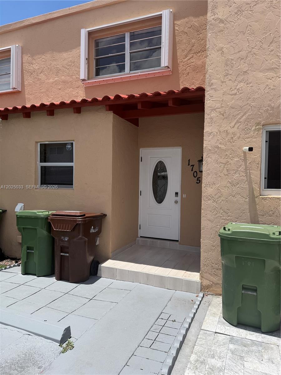 The exterior of a two-story stucco townhouse features a white front door and trash bins — 1705 W 57th St # 506, Hialeah FL 33012, HIALEAH, FL