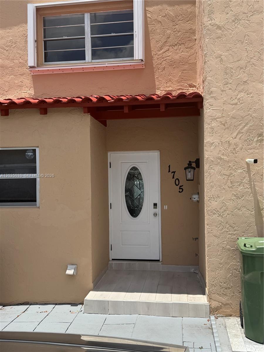 The exterior of a tan stucco townhouse features a white front door and red roof tiles — 1705 W 57th St # 506, Hialeah FL 33012, HIALEAH, FL