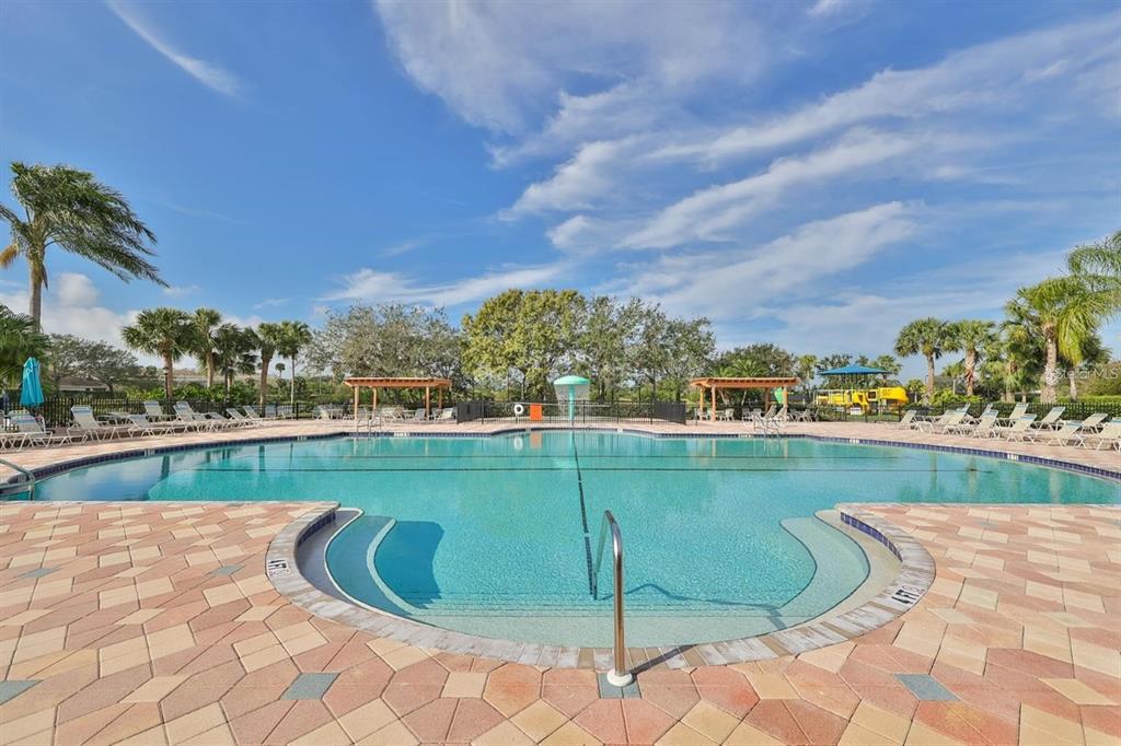 A large outdoor swimming pool with a paved deck, lounge chairs, and palm trees — 819 FAIRWAYCOVE LANE UNIT 102, BRADENTON, FL