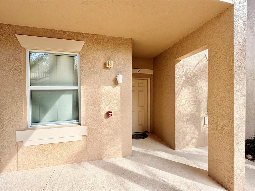 The exterior view shows a tan stucco building entrance with a window and door 102 — 819 FAIRWAYCOVE LANE UNIT 102, BRADENTON, FL