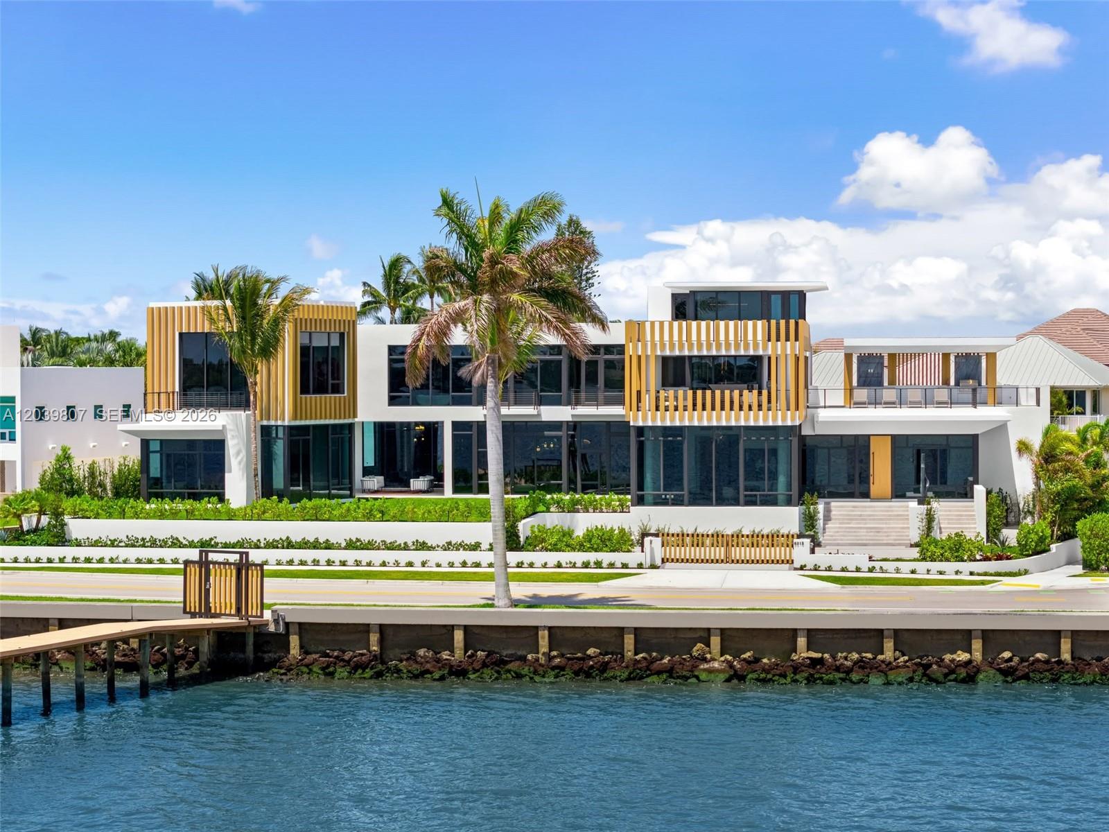 A modern multi-story waterfront home features large glass windows, wood-slat accents, and a palm tree — 6315 S Flagler Dr, West Palm Beach FL 33405, WEST PALM BEACH, FL