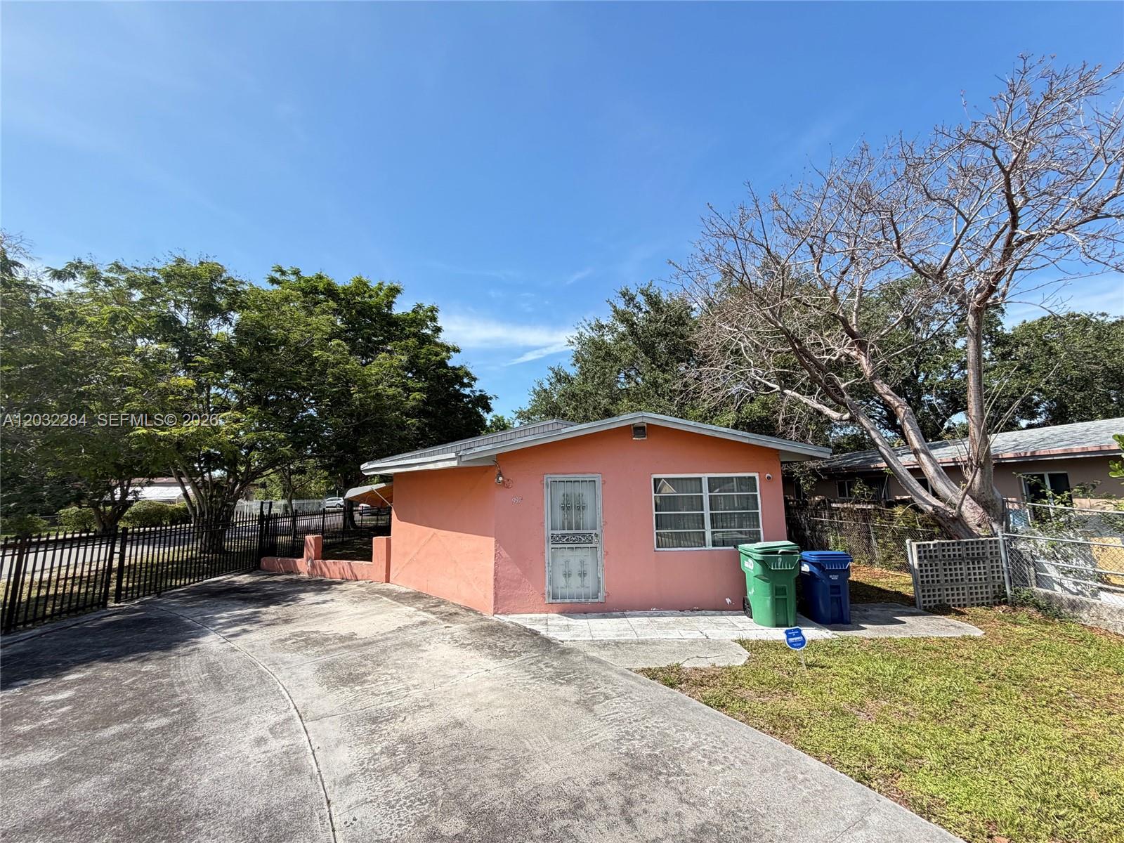A small, peach-colored house with a concrete driveway and two trash bins sits outside — 997 NW 116th St, Miami FL 33168, MIAMI, FL