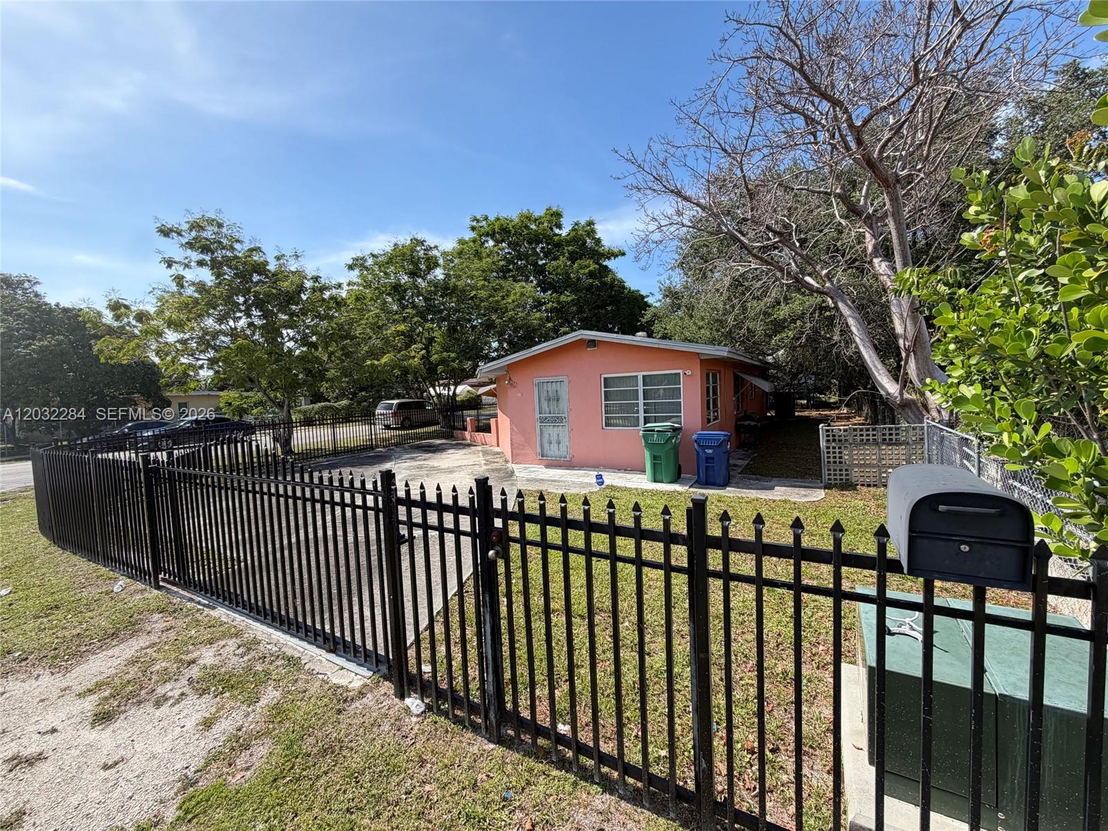 A pink single-story house sits behind a black metal fence with a paved driveway — 997 NW 116th St, Miami FL 33168, MIAMI, FL