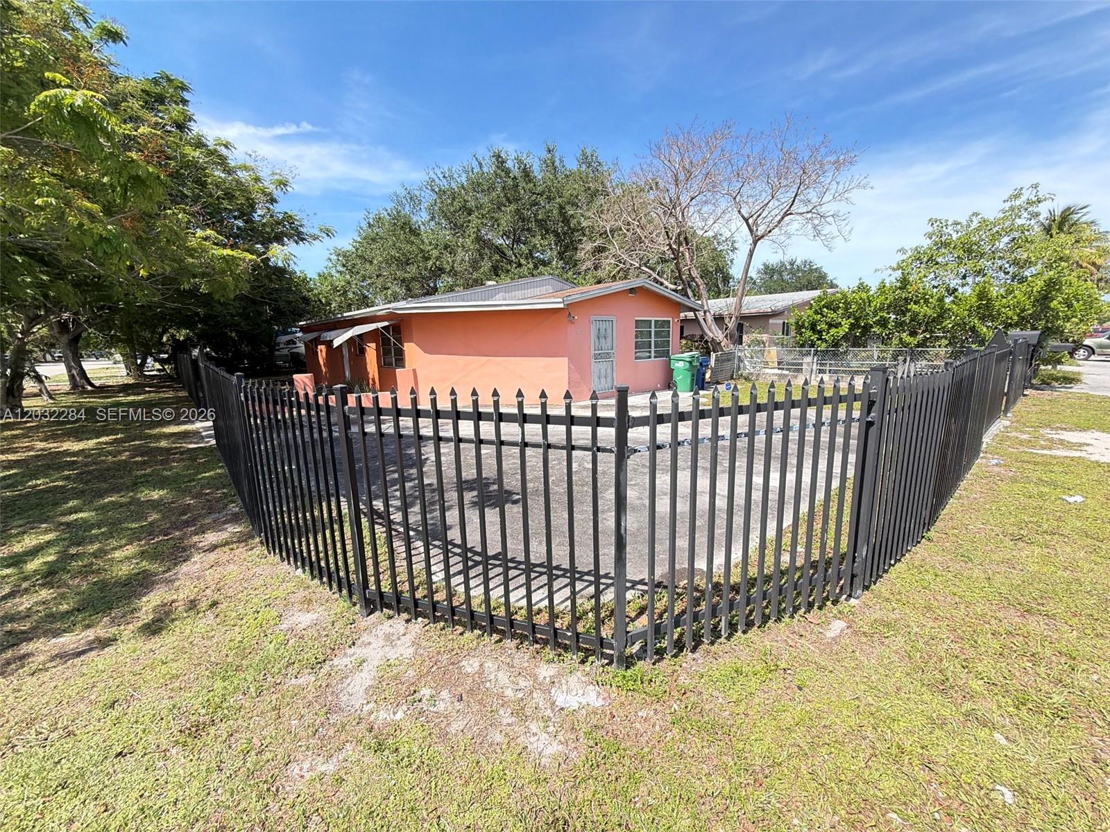 A peach-colored house is enclosed by a black metal fence on a grassy lot — 997 NW 116th St, Miami FL 33168, MIAMI, FL