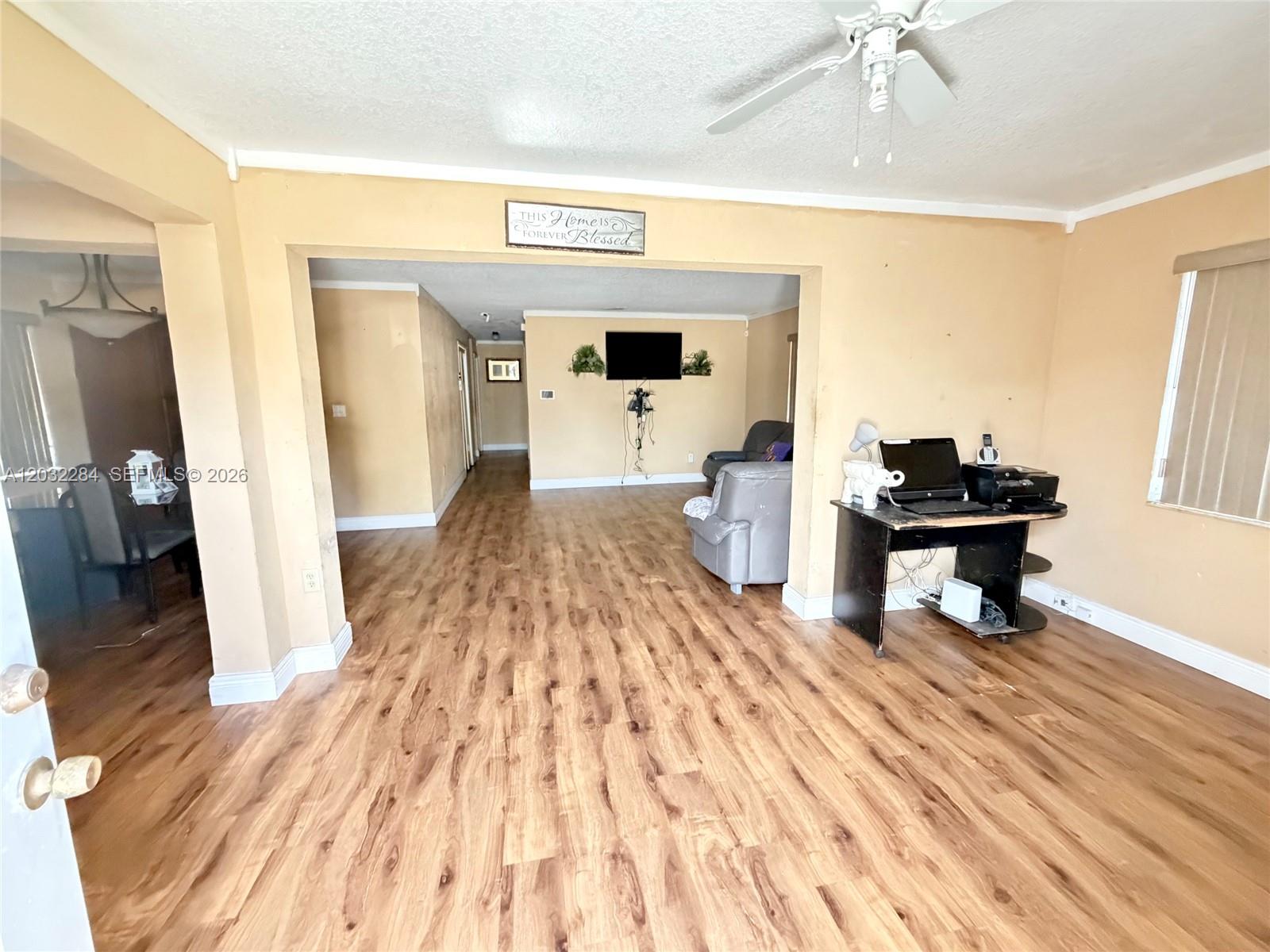 A living room features wood-look flooring, beige walls, and an open layout connecting two spaces — 997 NW 116th St, Miami FL 33168, MIAMI, FL