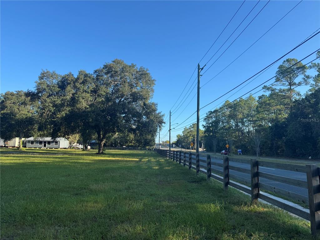 A grassy lot features a wooden fence along a road with trees and utility poles — TBD NE US HIGHWAY 301, WALDO, FL