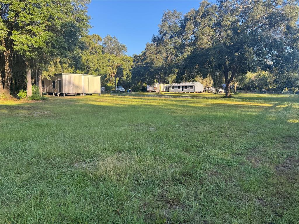 A large, grassy lot features a metal shed and a mobile home under mature trees — TBD NE US HIGHWAY 301, WALDO, FL