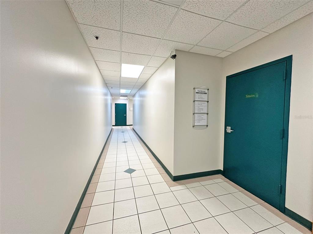 A long office hallway with white tiled floors, drop ceilings, and teal-colored doors — 7802 KINGSPOINTE PARKWAY UNIT 210, ORLANDO, FL