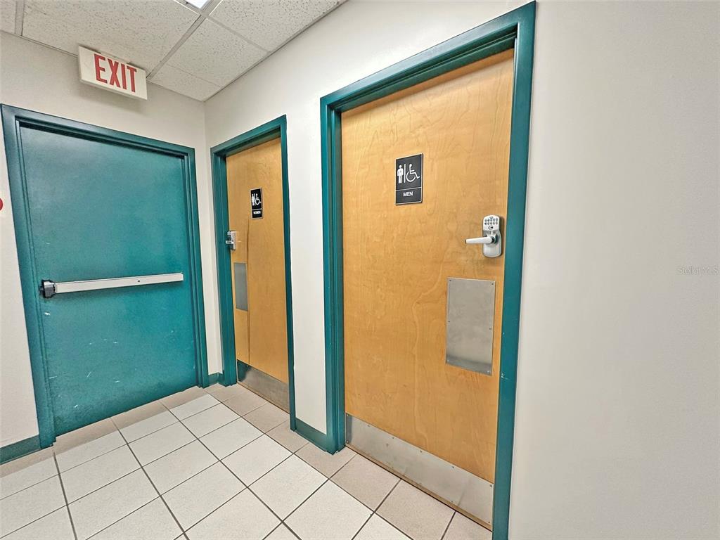 A hallway features an exit door and two restroom doors with light wood finishes — 7802 KINGSPOINTE PARKWAY UNIT 210, ORLANDO, FL