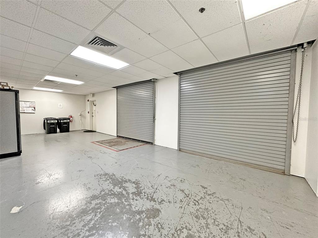 An industrial space features a gray concrete floor, two roll-up metal doors, and drop ceilings — 7802 KINGSPOINTE PARKWAY UNIT 210, ORLANDO, FL