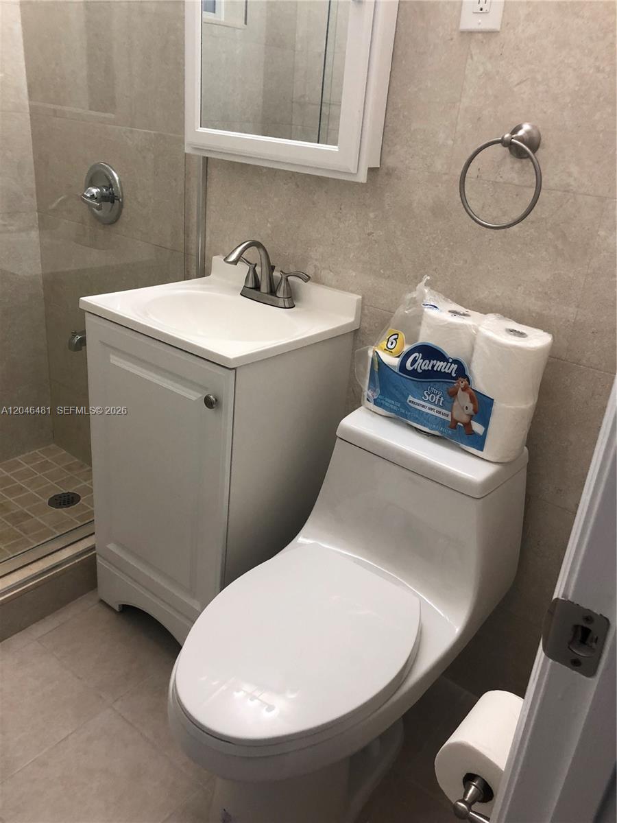 A small bathroom features a white vanity, a toilet with toilet paper, and a glass shower — 4440 NW 3rd St # 1, Miami FL 33126, MIAMI, FL