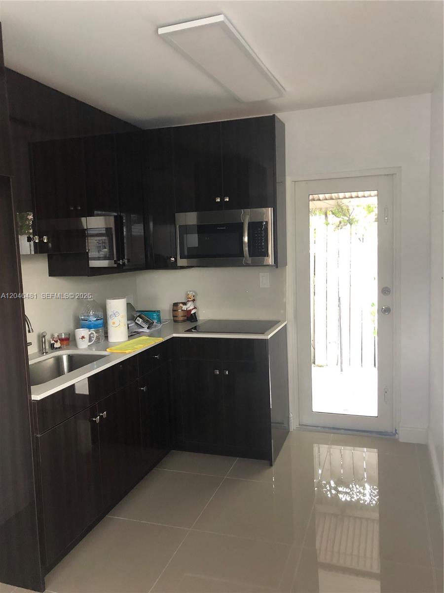 A kitchen features dark glossy cabinets, stainless steel appliances, white countertops, and a glass door — 4440 NW 3rd St # 1, Miami FL 33126, MIAMI, FL