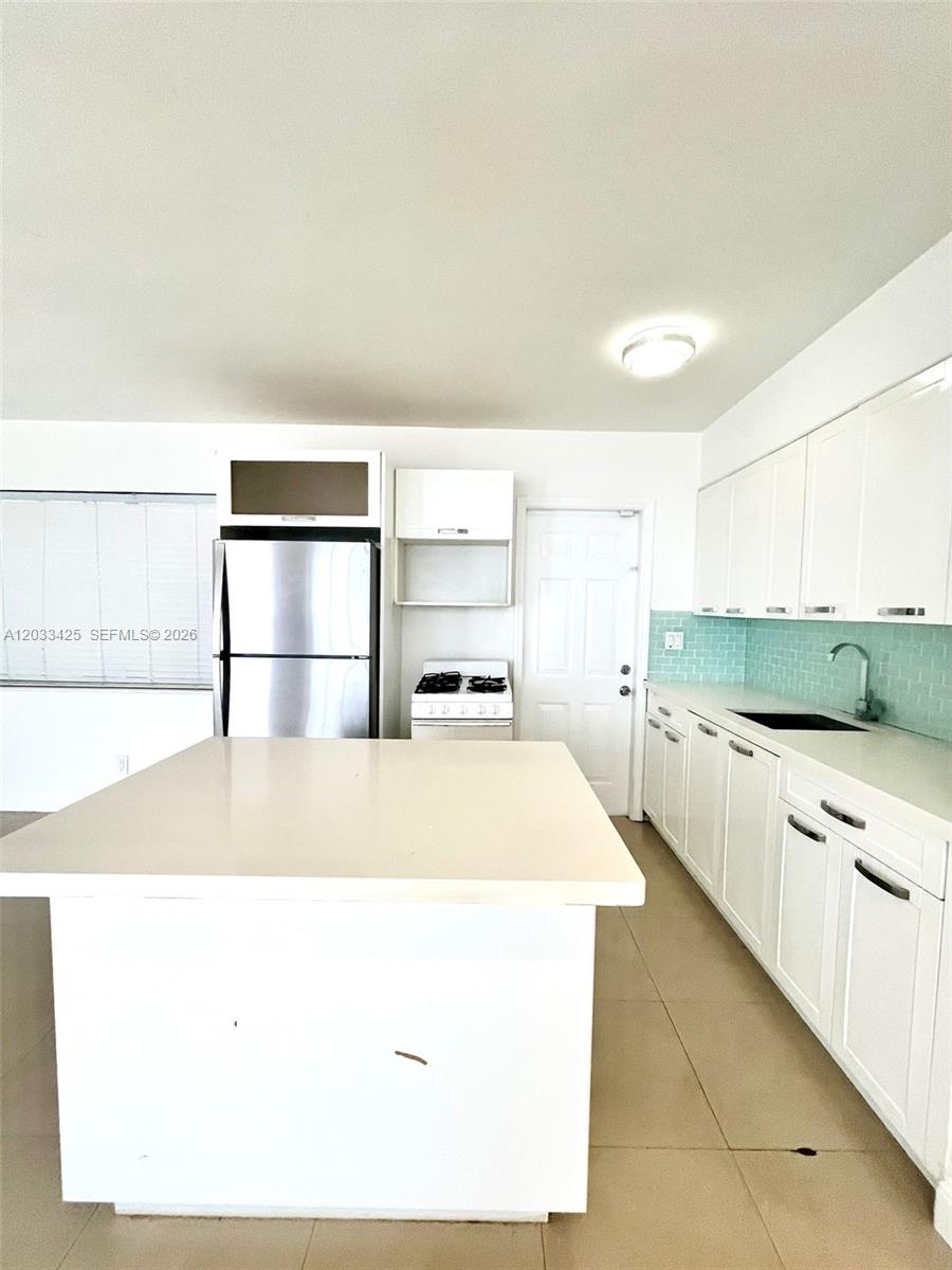 A kitchen features white cabinets, a central island, stainless steel appliances, and a light blue backsplash — 2031 Jackson St # 3, Hollywood FL 33020, HOLLYWOOD, FL