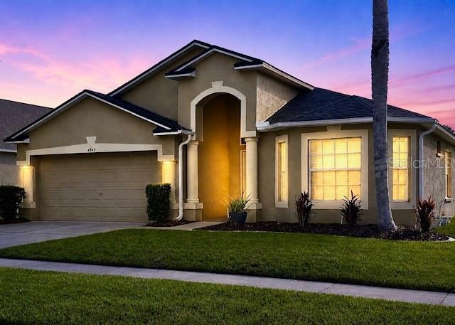 A single-story suburban house with a tan stucco exterior, a two-car garage, and a lawn — 4849 WESSEX WAY, LAND O LAKES, FL