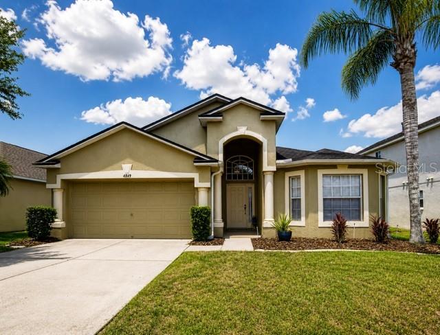 A single-story tan house with a two-car garage and a palm tree in the yard — 4849 WESSEX WAY, LAND O LAKES, FL