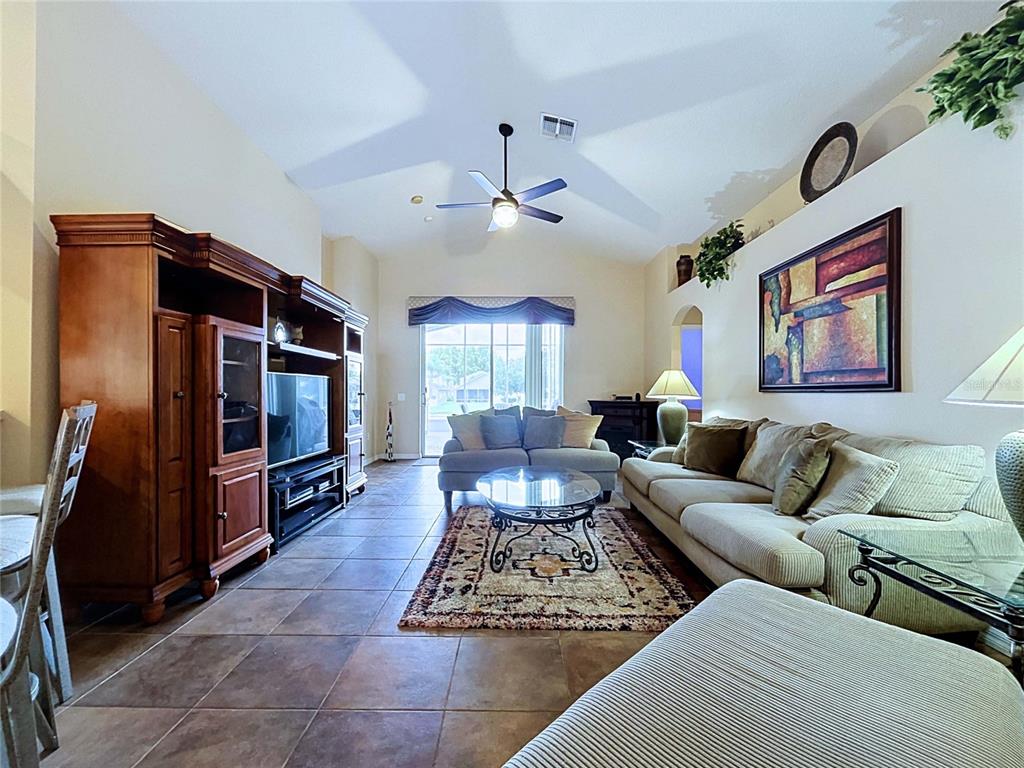 A living room features tile flooring, a vaulted ceiling with a fan, and wooden cabinetry — 4849 WESSEX WAY, LAND O LAKES, FL