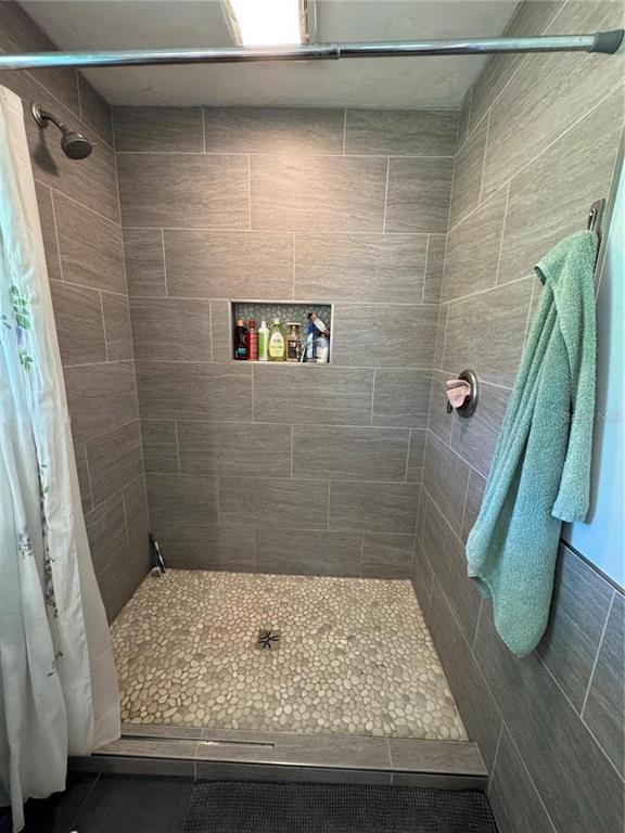 A walk-in shower features gray tile walls, a pebble-stone floor, and a built-in recessed niche — 3725 SW 162ND STREET, ARCHER, FL