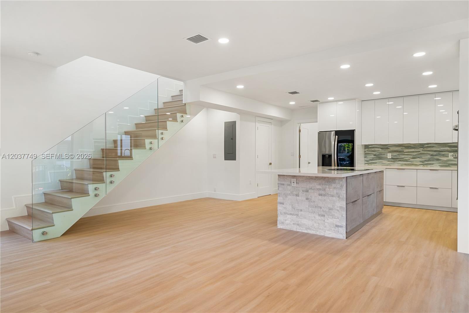 A modern kitchen features white cabinetry, a stone-accented island, and a glass-railed wooden staircase — 17 Coral Way, Key Largo FL 33037, KEY LARGO, FL