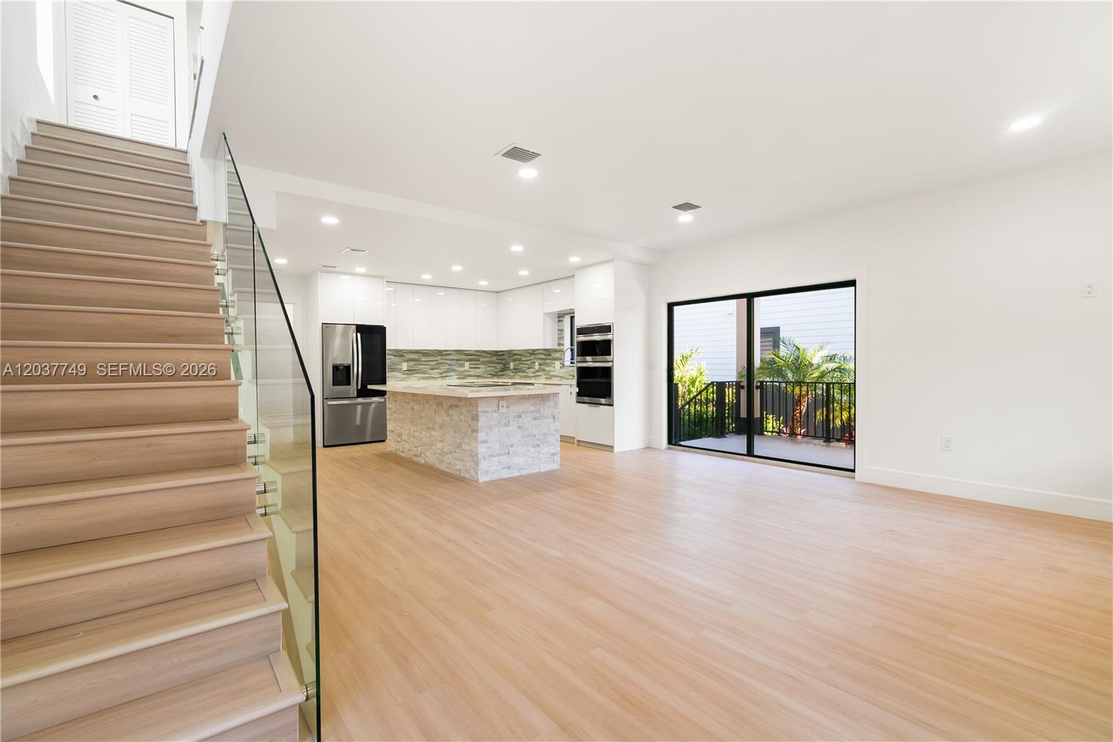 A modern kitchen with a stone island and stainless appliances sits beside a wooden staircase — 17 Coral Way, Key Largo FL 33037, KEY LARGO, FL
