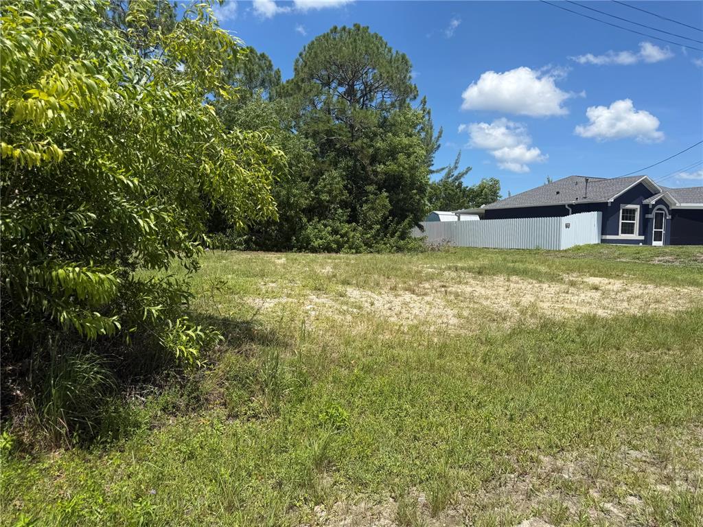 A vacant, grassy residential lot with trees and a neighboring house in the background — 2850 NW 28TH AVENUE, CAPE CORAL, FL