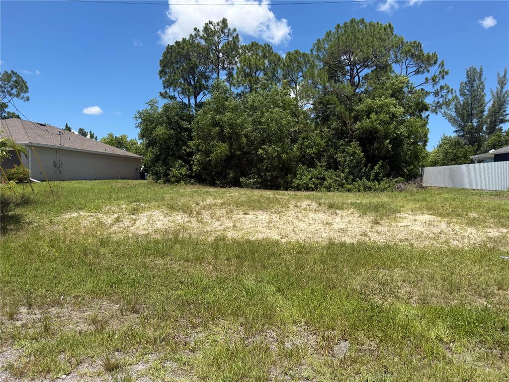 A vacant, grassy residential lot features a sandy patch and mature trees in the background — 2850 NW 28TH AVENUE, CAPE CORAL, FL