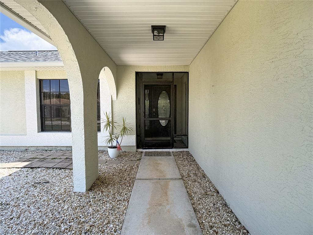 A covered entryway features a concrete walkway, arched columns, and a glass-paneled storm door — 9902 STEPHENSON DRIVE, NEW PORT RICHEY, FL