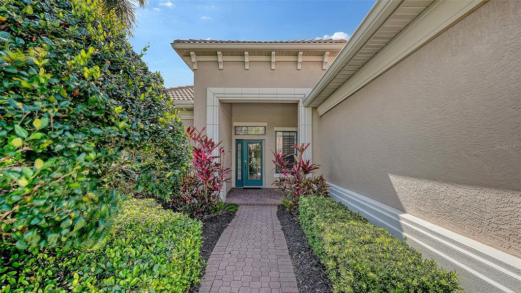 A paved walkway leads to the front entrance of a beige house with landscaping — 13911 SIENA LOOP, LAKEWOOD RANCH, FL