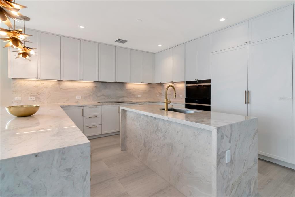A modern kitchen features white cabinetry, marble countertops, a waterfall island, and gold fixtures — 3101 W BAYSHORE BOULEVARD UNIT 804, TAMPA, FL