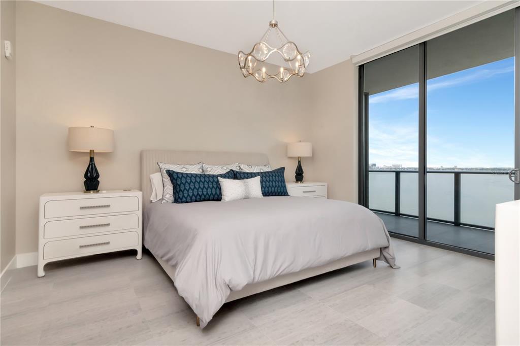 A bedroom features a bed with blue pillows, a chandelier, and a balcony overlooking water — 3101 W BAYSHORE BOULEVARD UNIT 804, TAMPA, FL