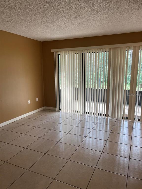 An empty room with tan walls, light-colored tile flooring, and vertical blinds covering a sliding door — 5109 EAGLESMERE DRIVE UNIT 11A, ORLANDO, FL