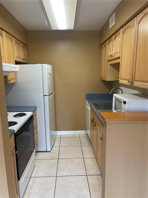 A galley kitchen features light wood cabinets, white appliances, and tiled flooring — 5109 EAGLESMERE DRIVE UNIT 11A, ORLANDO, FL