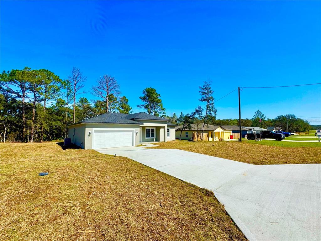 A single-story house with a white garage and concrete driveway sits on a grassy lot — 2085 W HAMPSHIRE BOULEVARD, CITRUS SPRINGS, FL