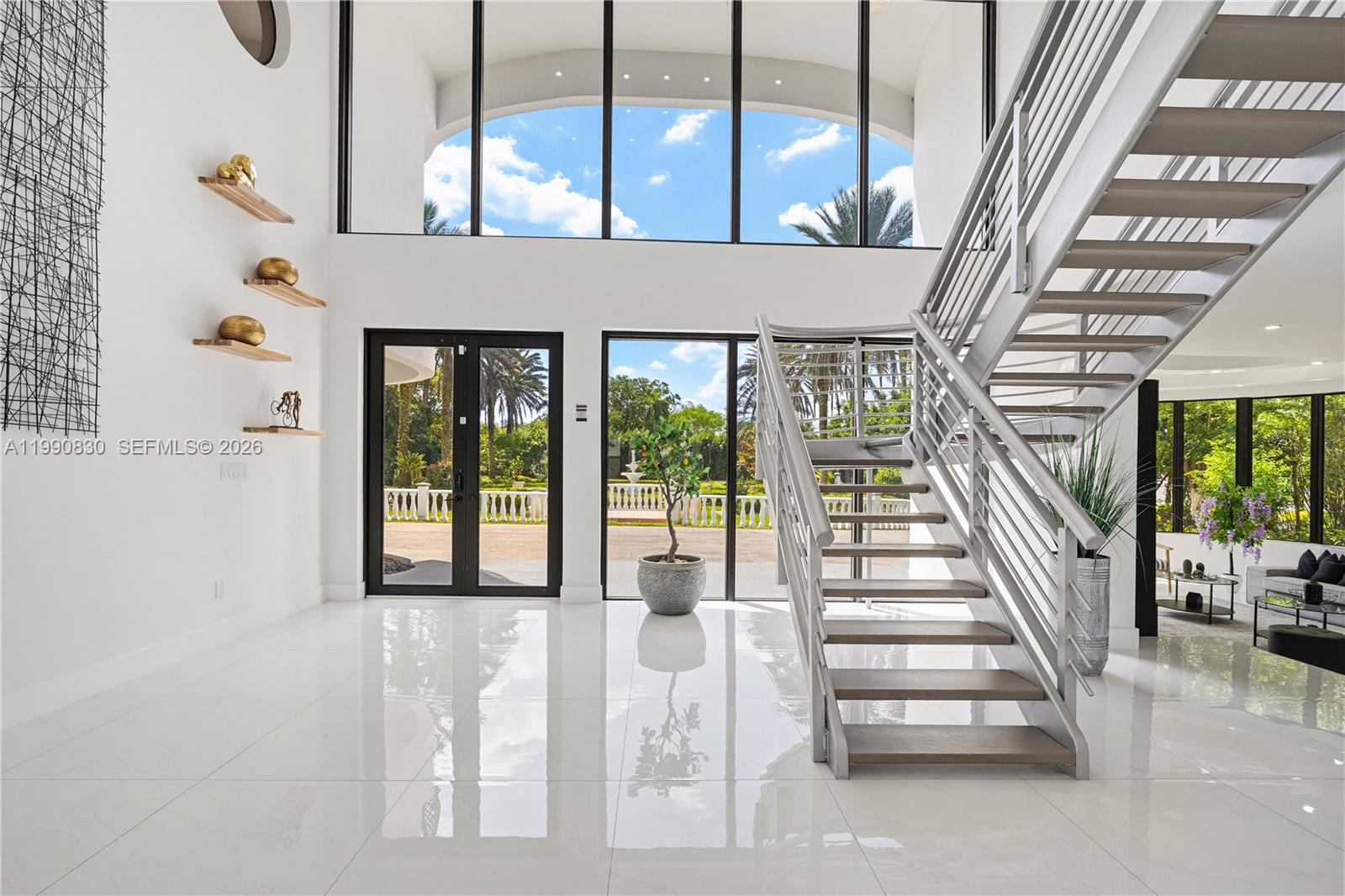 A bright, modern foyer features white tile floors, a floating staircase, and floor-to-ceiling windows — 14401 Sunset Ln, Southwest Ranches FL 33330, SOUTHWEST RANCHES, FL