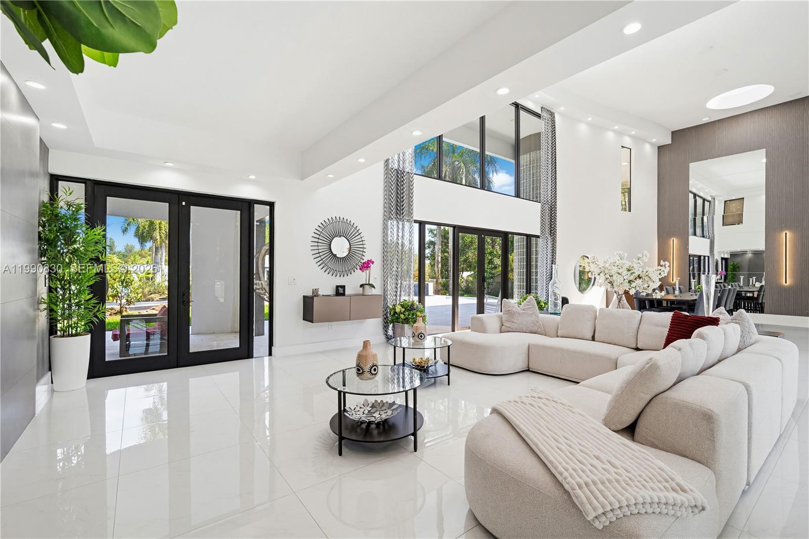 A bright, modern living room features white tile floors, a large sectional, and floor-to-ceiling windows — 14401 Sunset Ln, Southwest Ranches FL 33330, SOUTHWEST RANCHES, FL