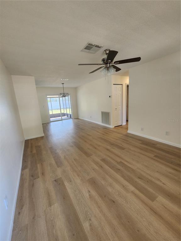 An empty living room features light wood-look flooring, a ceiling fan, and sliding glass doors — 13010 CUMBERLAND DRIVE, LARGO, FL