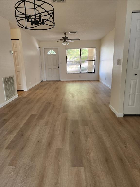 An empty living room features light wood-look flooring, a ceiling fan, and a modern chandelier — 13010 CUMBERLAND DRIVE, LARGO, FL