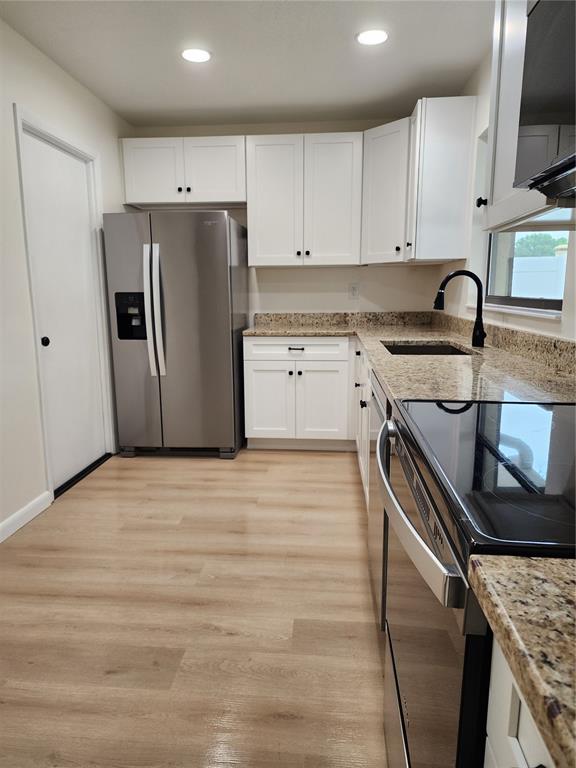 A kitchen features white cabinets, granite countertops, stainless steel appliances, and light wood-look flooring — 13010 CUMBERLAND DRIVE, LARGO, FL