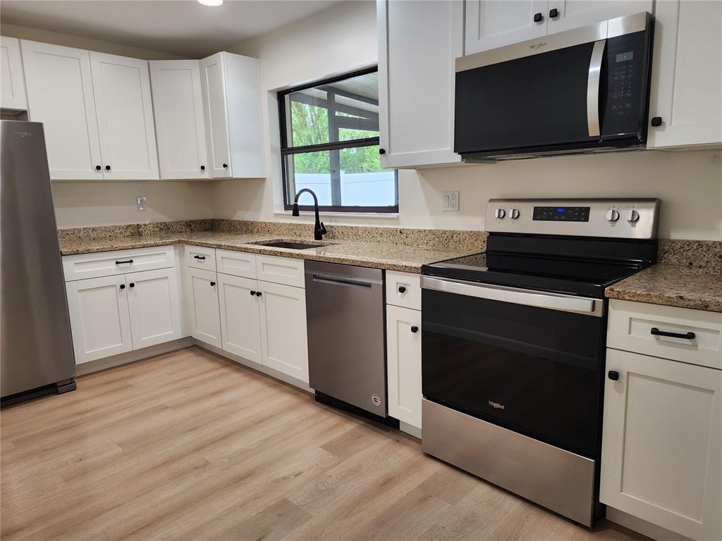 A kitchen with white cabinets, stainless steel appliances, and tan granite countertops — 13010 CUMBERLAND DRIVE, LARGO, FL
