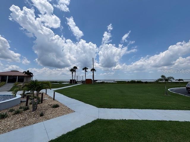 A grassy lawn leads to a waterfront view with palm trees and a building nearby — 1018 CALENDULA DRIVE, INDIAN LAKE ESTATES, FL
