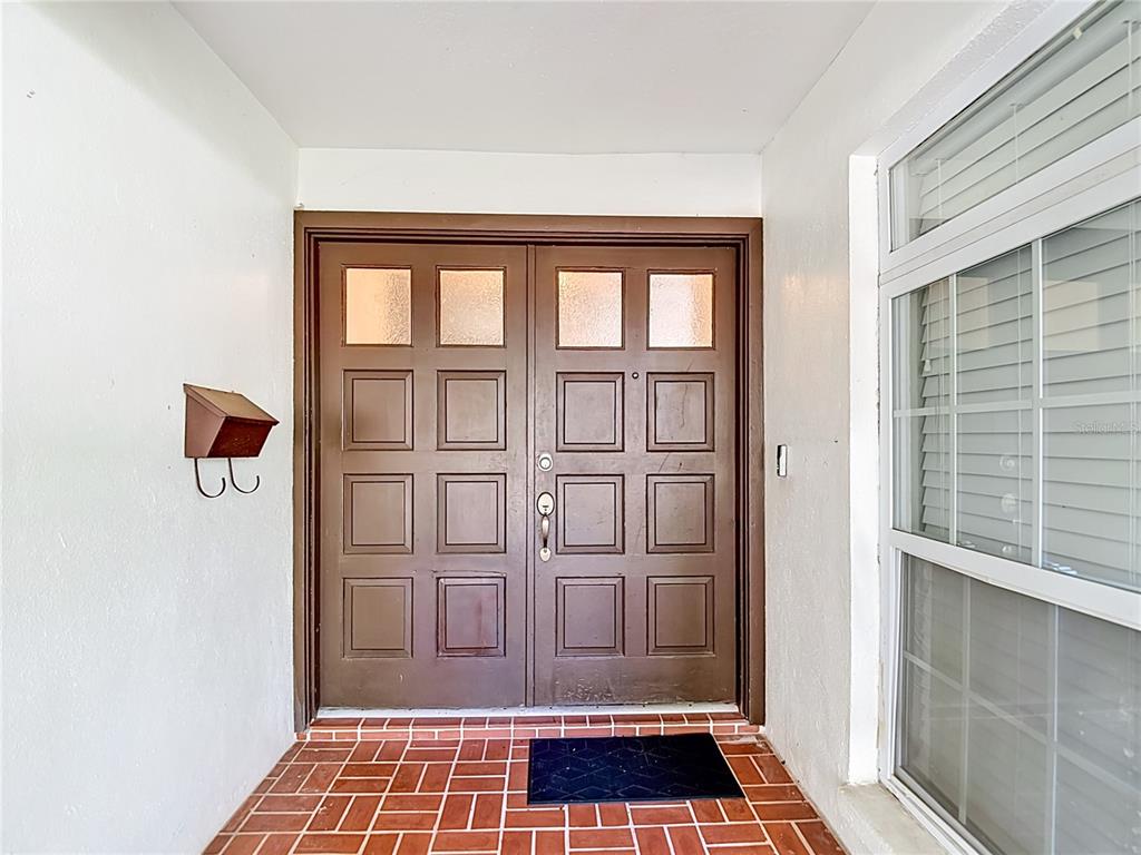A brown double front door with glass panels sits on a red brick porch — 5126 ROLLING HILLS COURT, TAMPA, FL