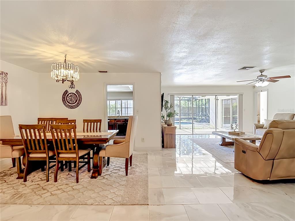 A dining area with a chandelier and a living room with tile floors and sliding doors — 5126 ROLLING HILLS COURT, TAMPA, FL