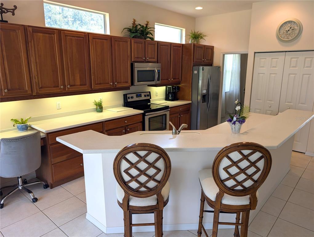 A kitchen features wood cabinets, white countertops, a breakfast bar with two chairs, and stainless appliances — 4406 REFLECTIONS PARKWAY, SARASOTA, FL