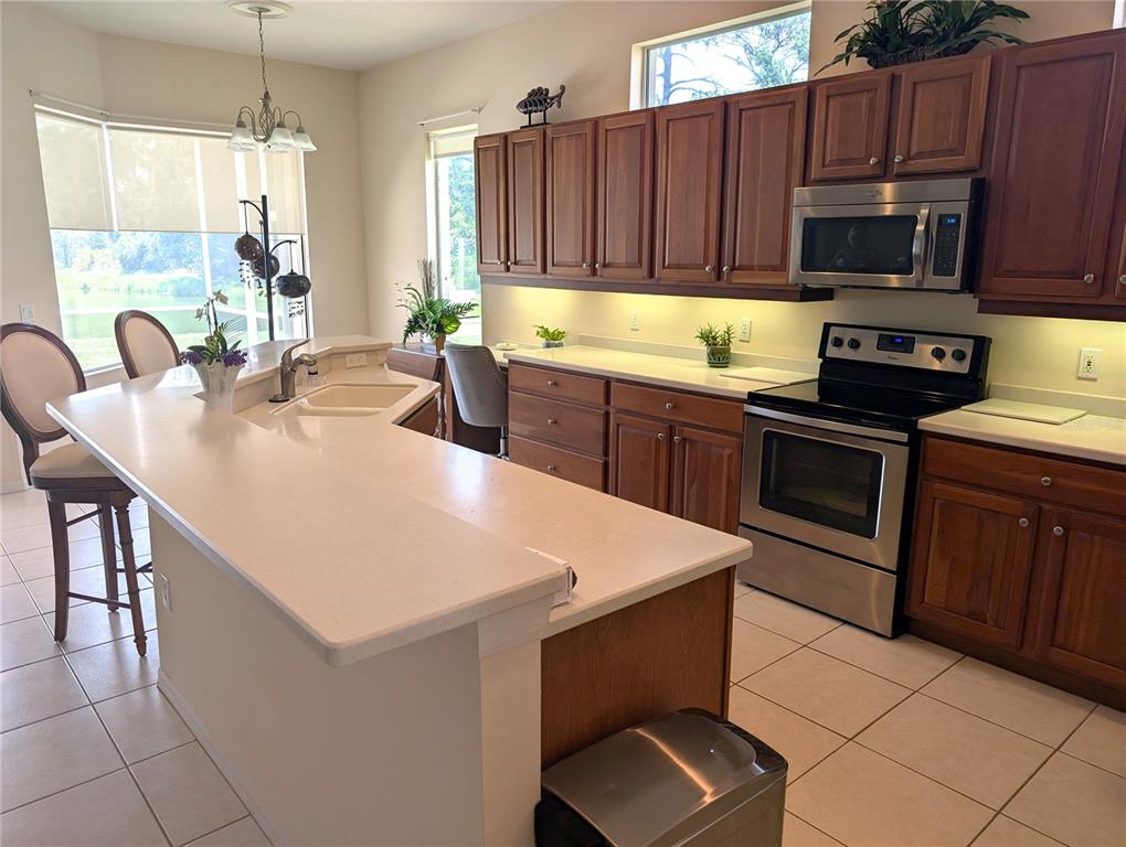 A kitchen features wood cabinets, stainless steel appliances, a breakfast bar, and tile flooring — 4406 REFLECTIONS PARKWAY, SARASOTA, FL